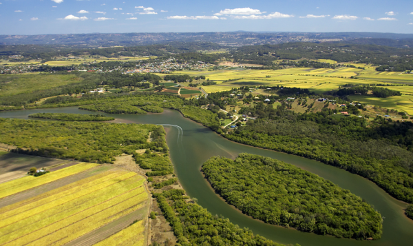 Meandering River Through Agricultural Landscape A meandering river flowing through farmland, with bush along the banks, hills in the distance, and scattered white clouds in a blue sky.