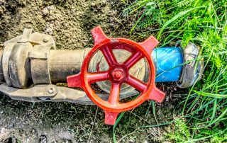 Red irrigation shut-off valve on an underground water pipe surrounded by soil and grass.